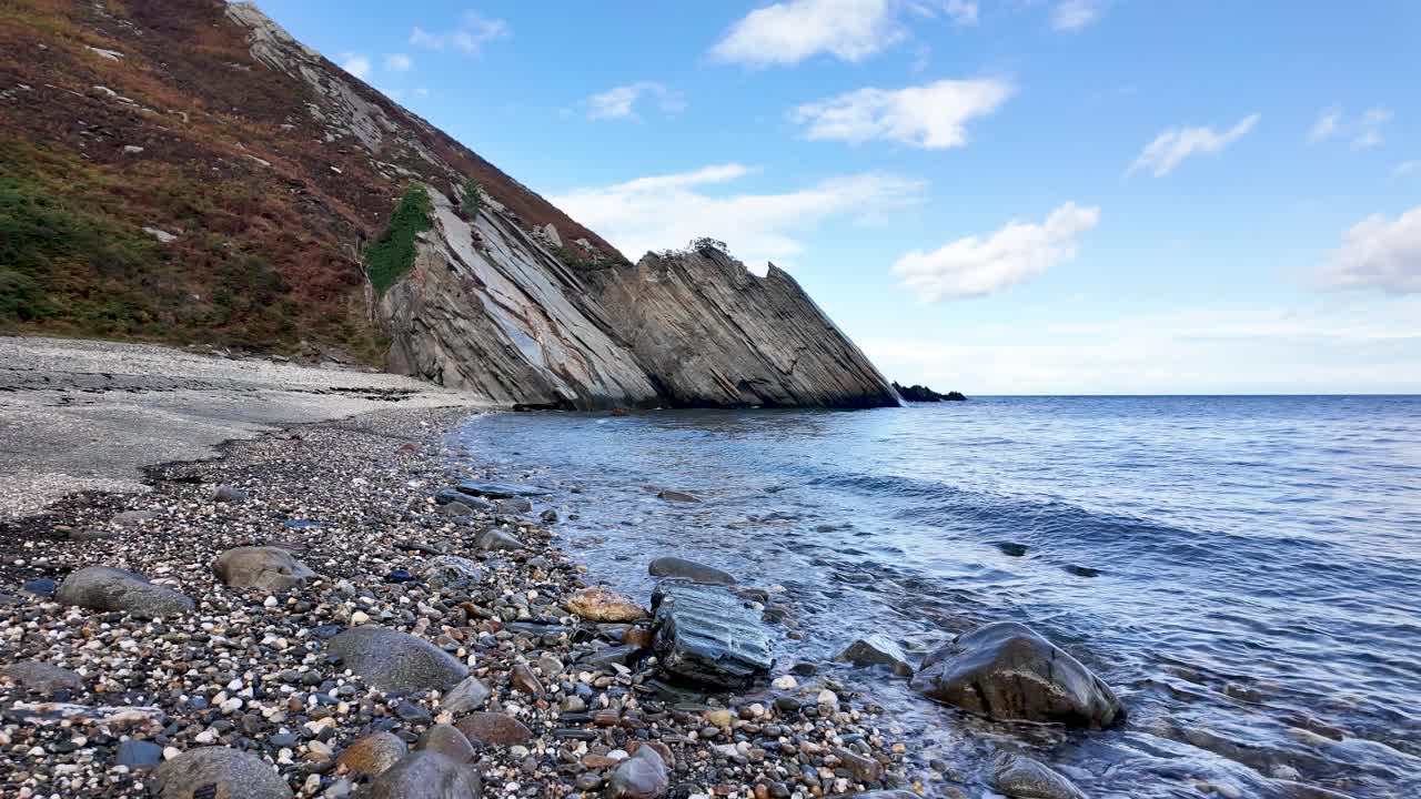 Dhoon beach showing pebbles, sea, and stratified rock formations under a blue sky