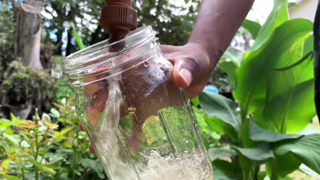 African-Male-filling-glass-jar-with-water-from-tap