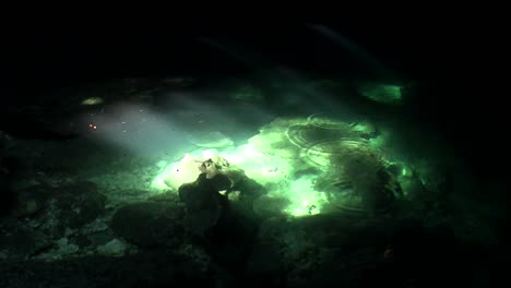 green pools glimmer in the sunlight at the bottom of a cave