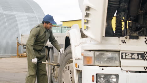 trabajador con mono verde arreglando un camión en un parque logístico