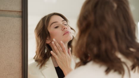 Curious-redhead-woman-touches-soft-facial-skin-after-makeup