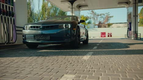 Close-up-shot:-a-beautiful-glossy-dark-gray-convertible-pulls-into-a-gas-station.-The-car-is-approaching-the-camera,-view-from