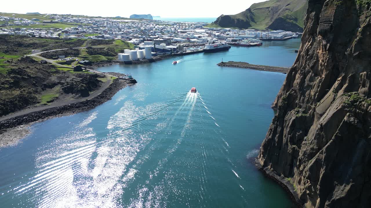 Zodiac boat sailing through calm blue shimmering water towards the harbor, passing by rough edge cliffs