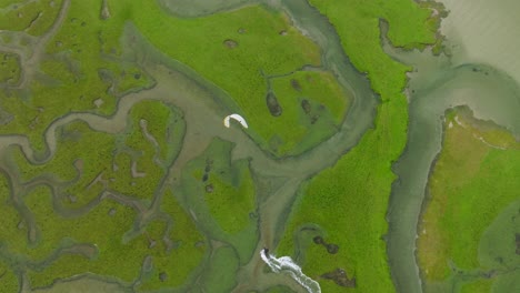 wide aerial birdseye view of a kitesurfing adventurer sailing through a bright green river delta on the island of achill in ireland