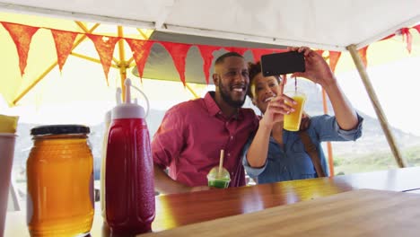 pareja feliz diversa sonriendo y tomando selfies en el mostrador del camión de comida