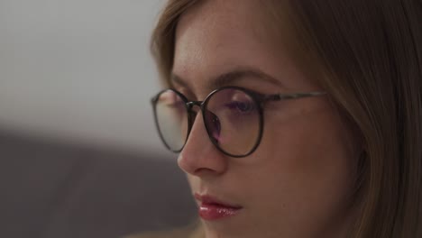 primer plano de una mujer con gafas que bloquean la luz azul viendo la televisión