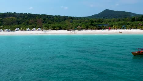 Aerial-reveal-of-white-sand-beach-with-blue-sea-and-long-tail-boat