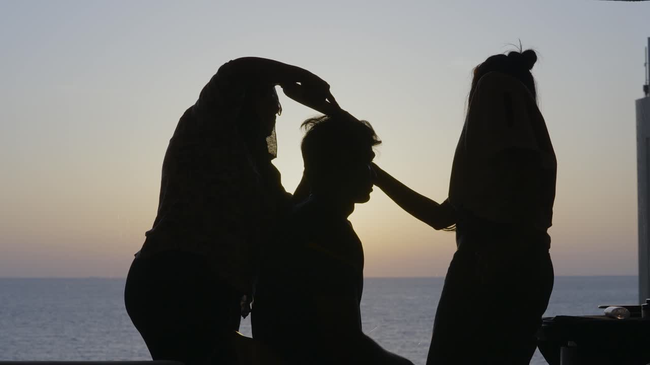 Silhouette of a man having makeup and hair done while the sun is setting