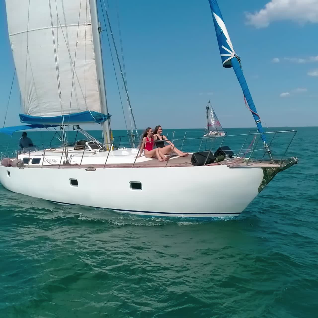 Young women relaxing on a white yacht. Luxury sailboat floating on the sea water on the city background. Sea voyage in summer day. Camera rising