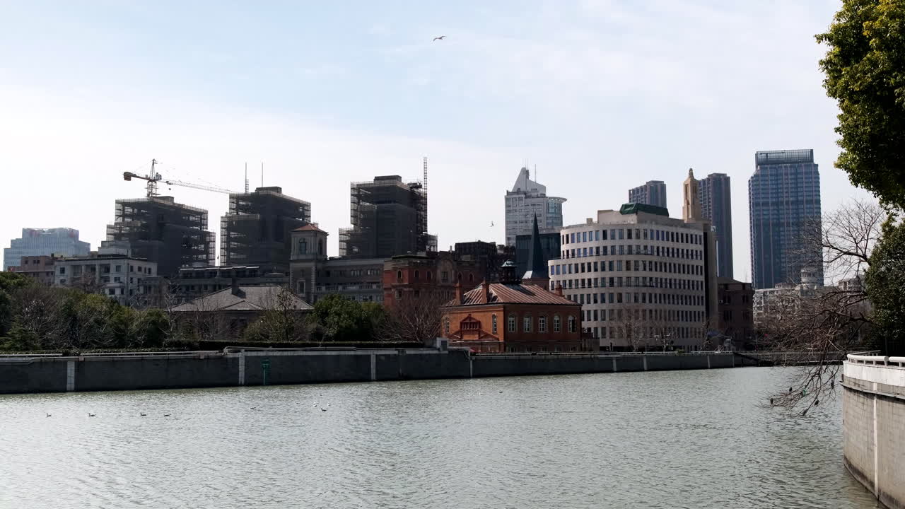 Shanghai waterfront with a mix of historic buildings, modern structures, and several high-rises under construction