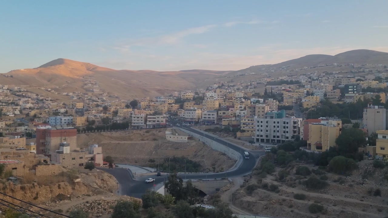 La luce del mattino rivela la città desertica di Wadi Musa, Giordania, con viste panoramiche su colline aspre, strade polverose e la porta d'accesso all'antica città di Petra sotto cieli sereni e soleggiati