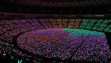 a mesmerizing display of colorful lights fills the stadium, showcasing the vibrant energy of the crowd as participants wave glowing sticks in rhythm, creating an electric atmosphere