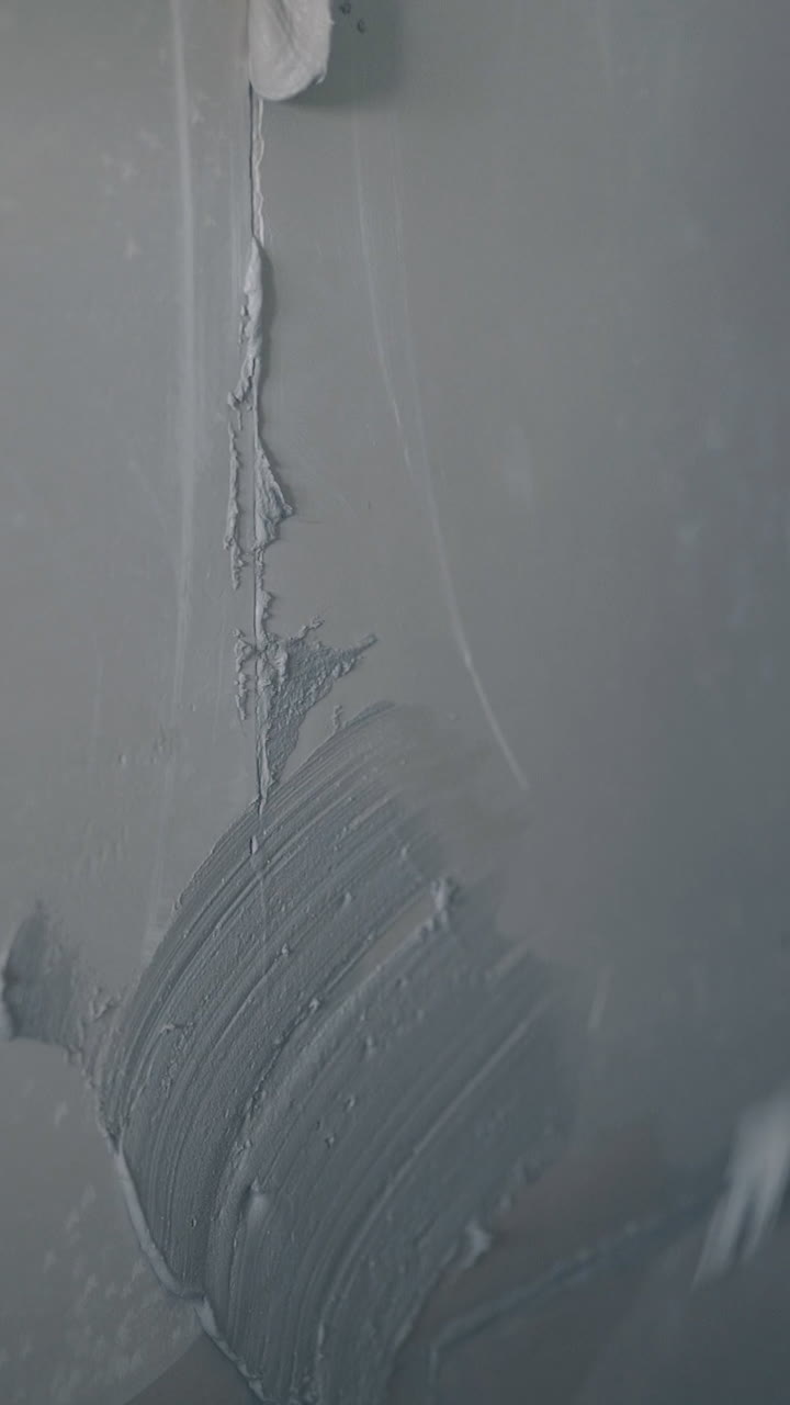 professional painter arm in blue sweatshirt and gloves holds putty knife and smears wall with primer closeup