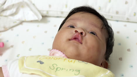 asian newborn girl, contentedly lying on a bed with drool, expressing joy and early life development. ideal for illustrating tender moments and baby care.