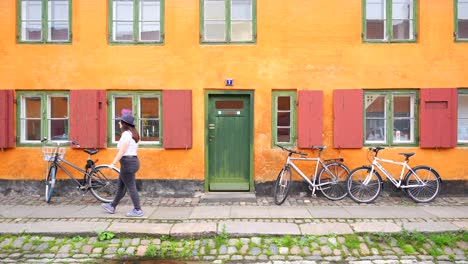 woman walking in front of nyboder colorful yellow house with parked bikes on cobbled street, copenhagen