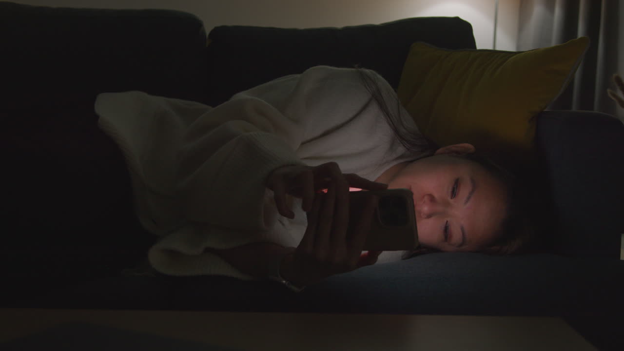 Woman Spending Evening At Home Lying On Sofa With Mobile Phone Scrolling Through Internet Or Social Media 13