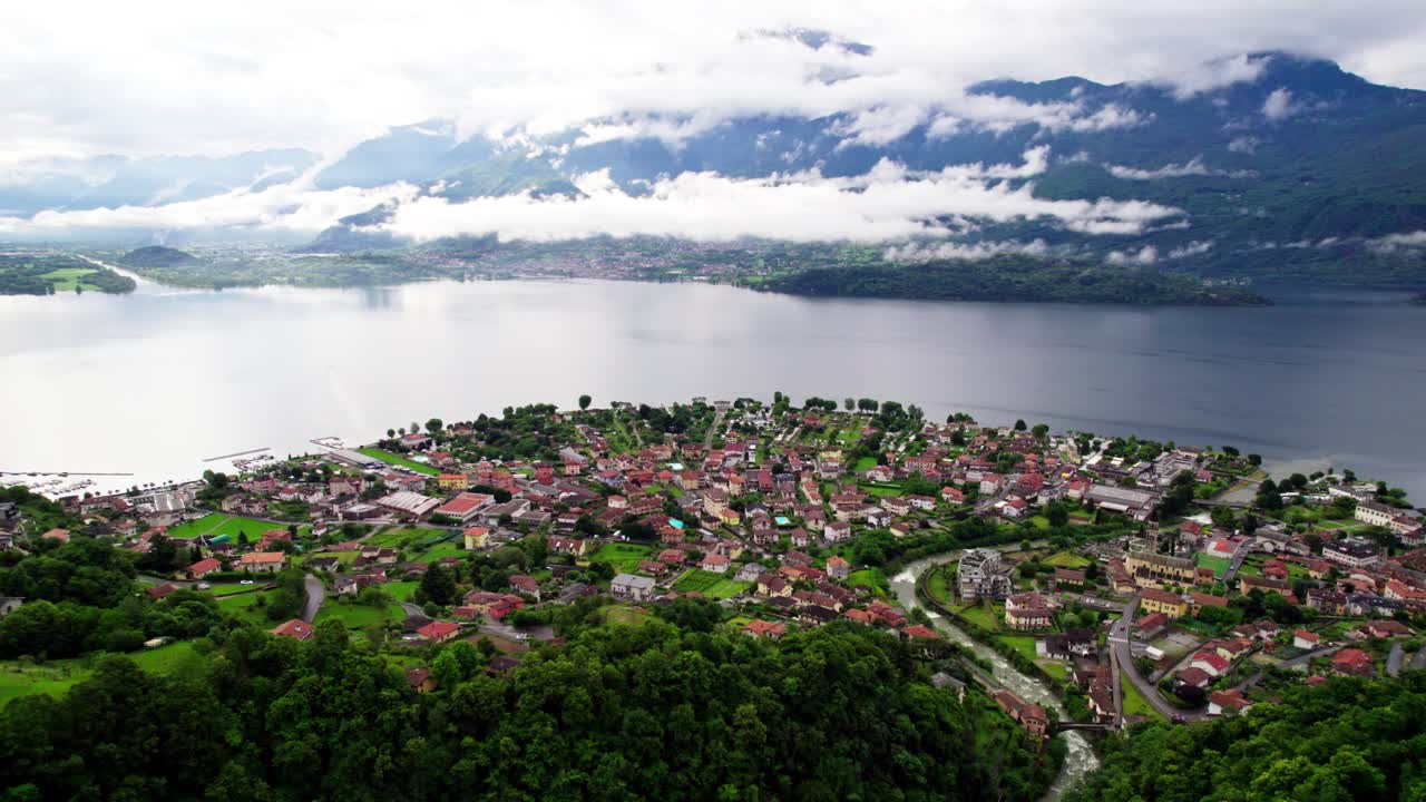 Filmato aereo cinematografico realizzato con drone che vola all'indietro sopra una città storica con tetti rossi, rivelando il Lago di Como e una grande montagna alpina sullo sfondo