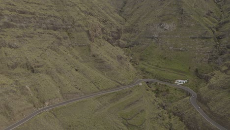 Panorama-drone-shot-of-a-car-driving-through-a-curvy-road-in-a-canyon-with-mountains