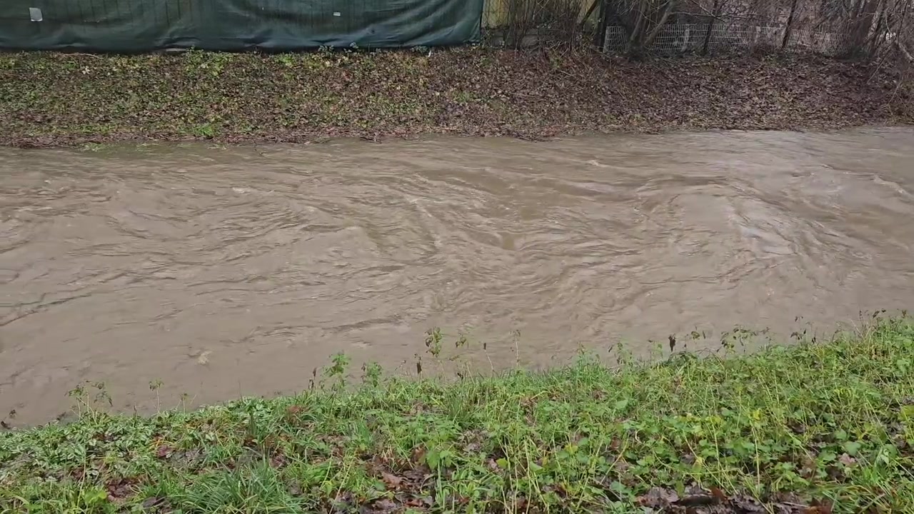 Raging muddy river water flowing rapidly after heavy rainfall, showing the force of nature