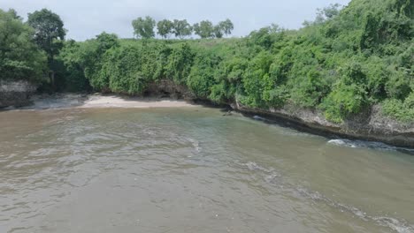 Low-altitude-dolly-aerial-drone-shot-over-polluted-sewage-water-and-floating-trash-with-debris-over-dead-coral-reef-mixing-with-turquoise-water-and-tropical-coastine-in-Bali-Indonesia