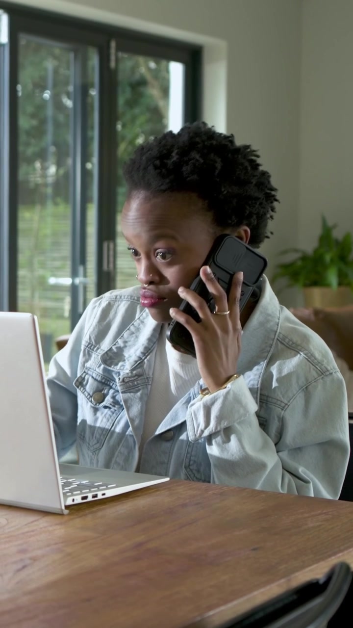 Vertical video: Sipping pink mug, woman typing on laptop calling phone working at home in denim