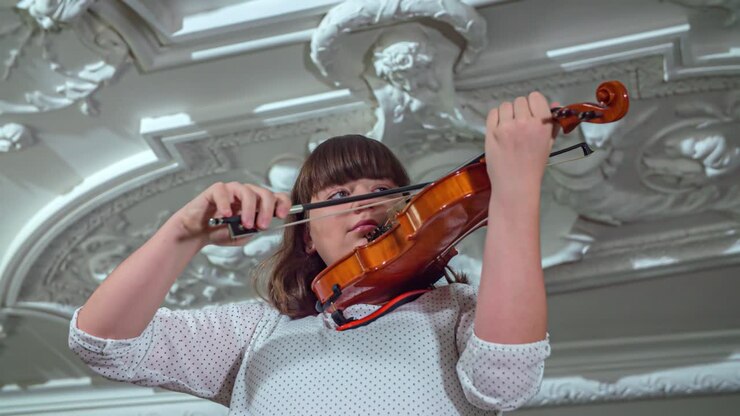 Young Caucasian woman plays the violin inside building, slow motion, low angle pan