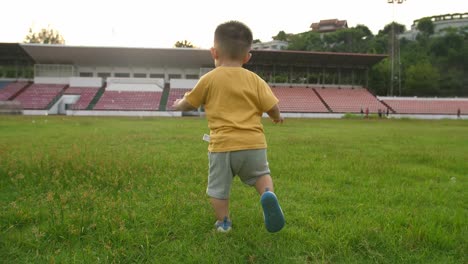 a toddler boy running on the grass at stadium