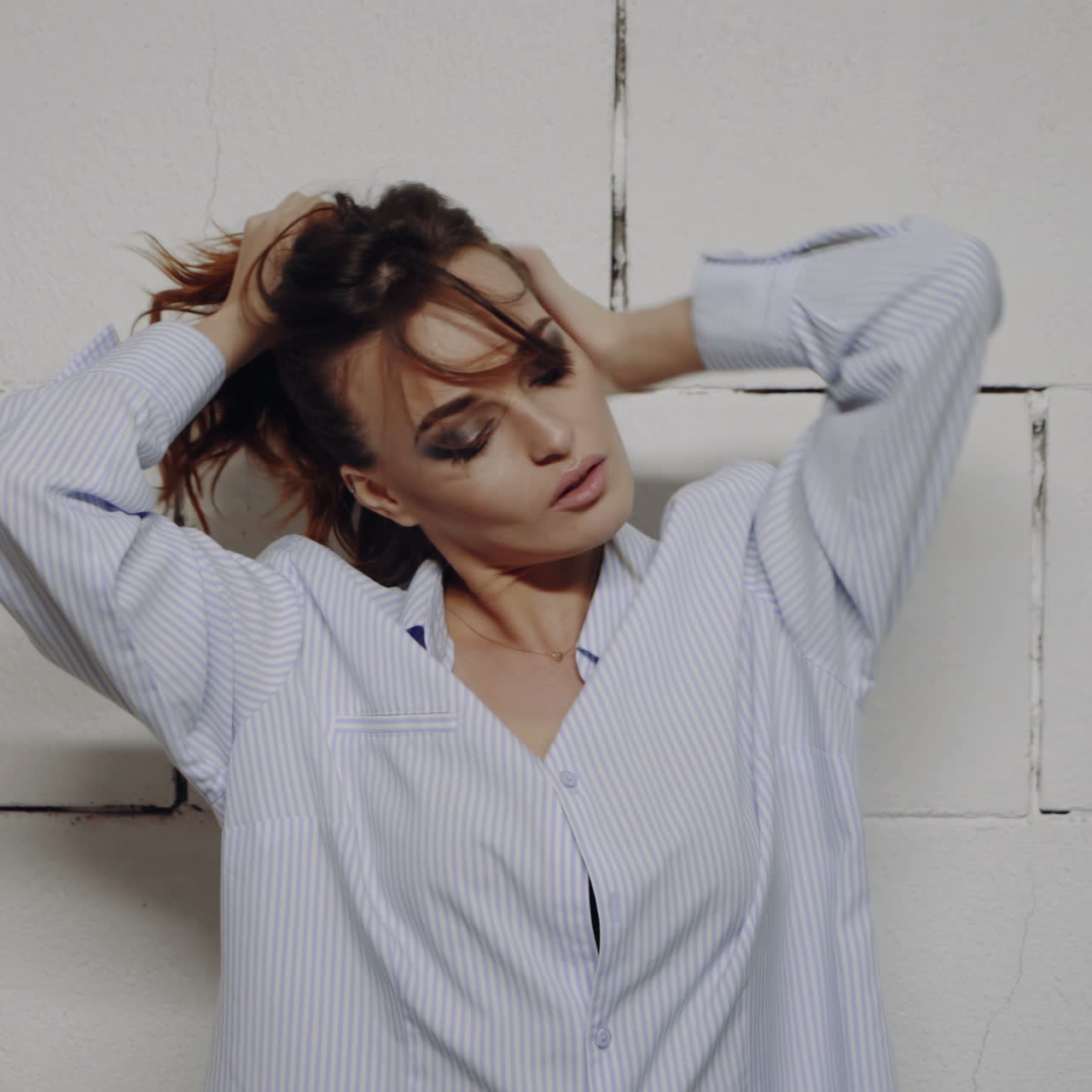 Donna in camicia a righe in posa davanti a un muro di mattoni
