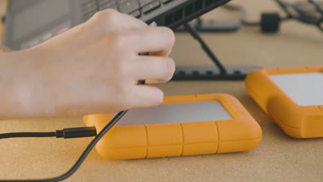 a hand connects an orange lacie hard drive to a pc