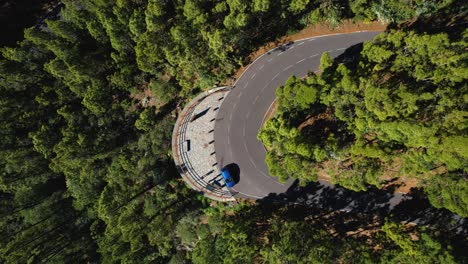 Birds-Eye-View-Of-A-Blue-Car-On-A-Curvy-Mountain-Road-With-Beautiful-Green-Trees