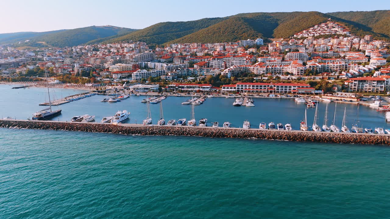 Flying over the blue seascape along dam with berth for boats. View on the sunny resort of Sveti Vlas, Bulgaria