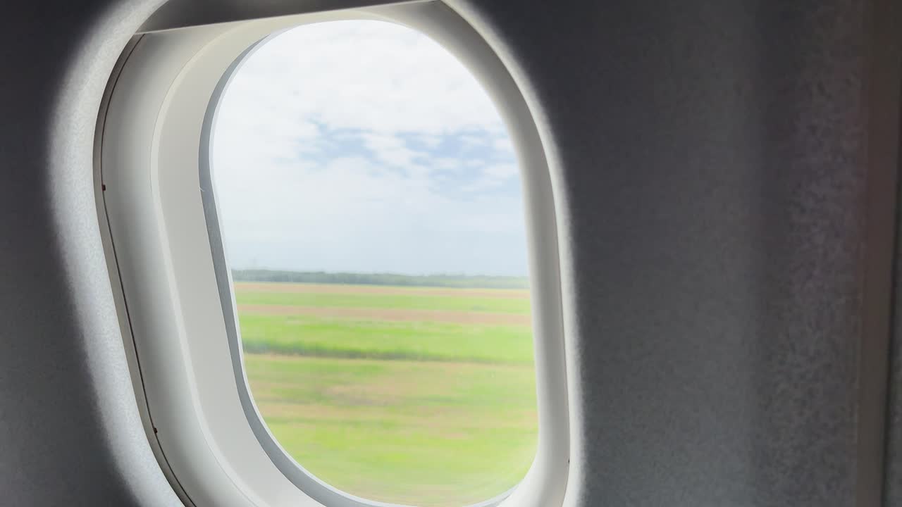 Aircraft moves along runway in daylight, green fields visible through window, steady camera, natural lighting
