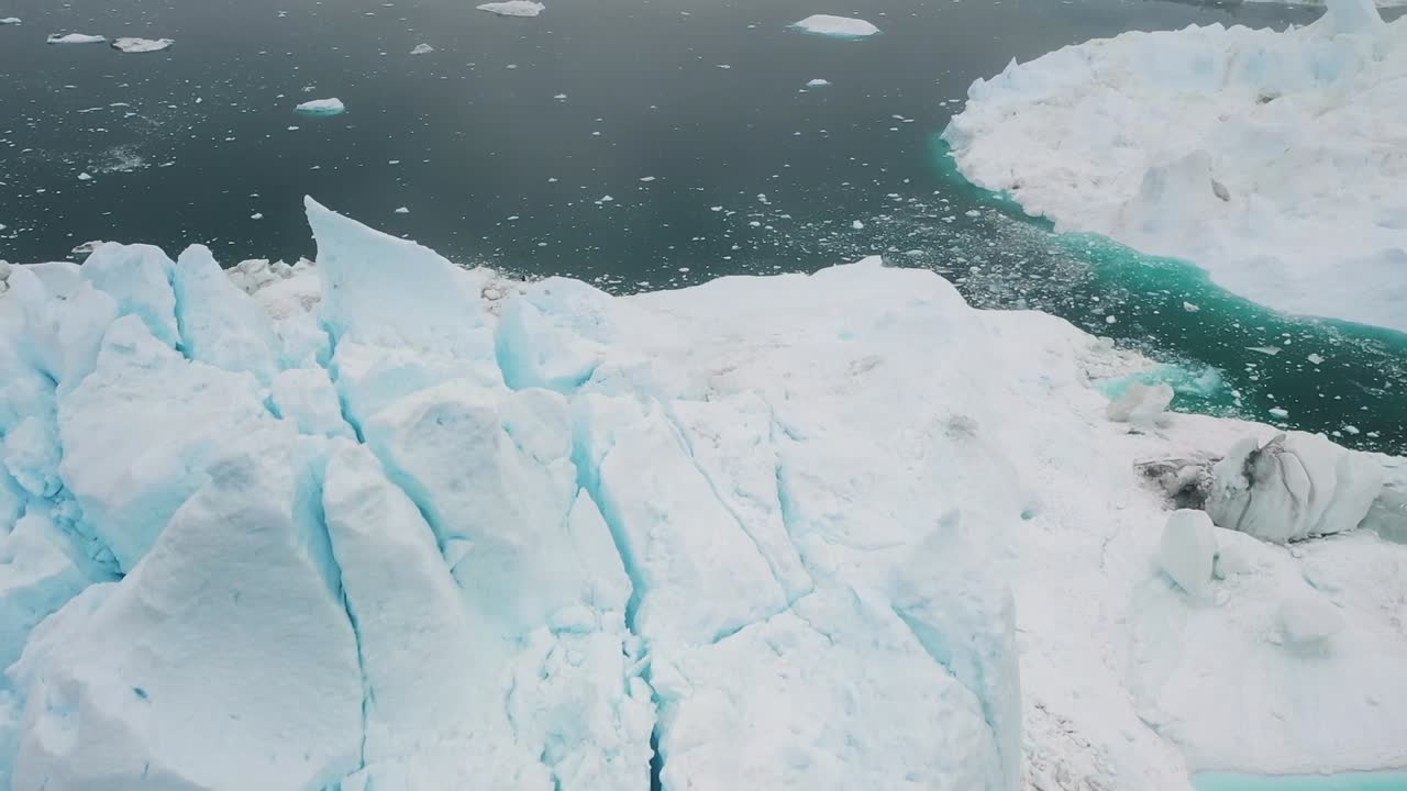 Aerial drone view of massive blue and white icebergs floating in the dark Arctic sea near Greenland, showcasing frozen beauty, icy textures, and calm polar environment