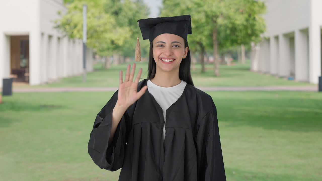 Felice ragazza indiana neolaureata che saluta la telecamera con la mano.