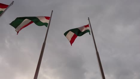 tres banderas húngaras en mástiles ondeando en el viento con nubes de tormenta en el fondo - cámara lenta disparada mirando hacia arriba