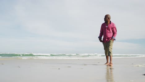 african american senior man walking on a beach looking at the sea