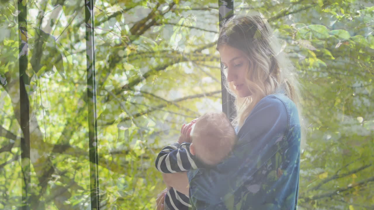Animation von Bäumen über einer glücklichen kaukasischen Mutter, die ihr Baby hält