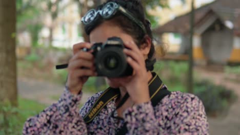 close-up frontal shot of indian woman photographer with a dslr camera taking photos as she looks thought the camera viewfinder