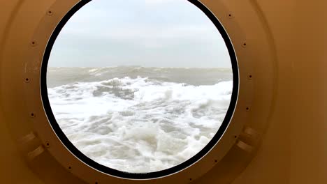 view through a porthole on a stormy sea with waves hitting the ship