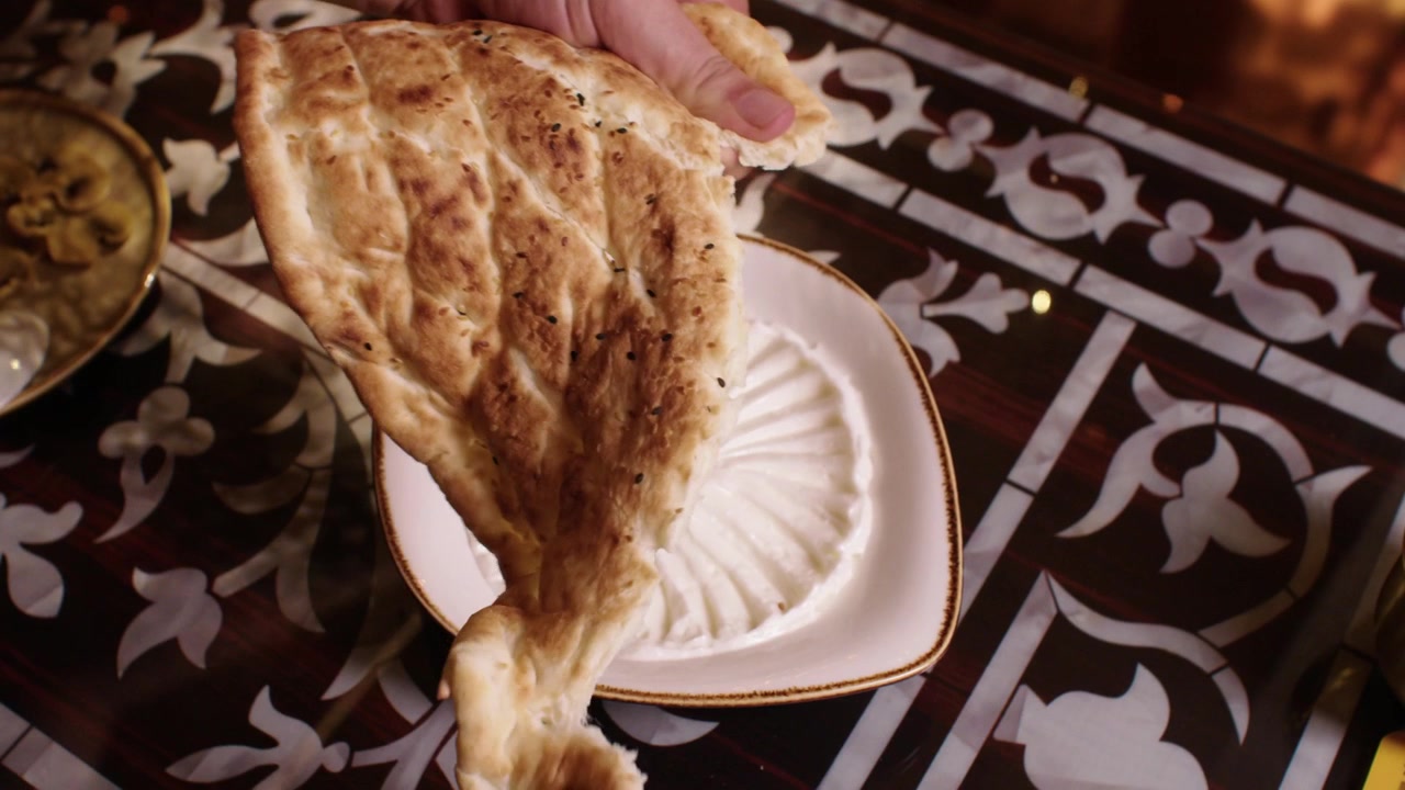 Person tearing freshly baked flatbread to eat with a traditional Middle Eastern appetizer