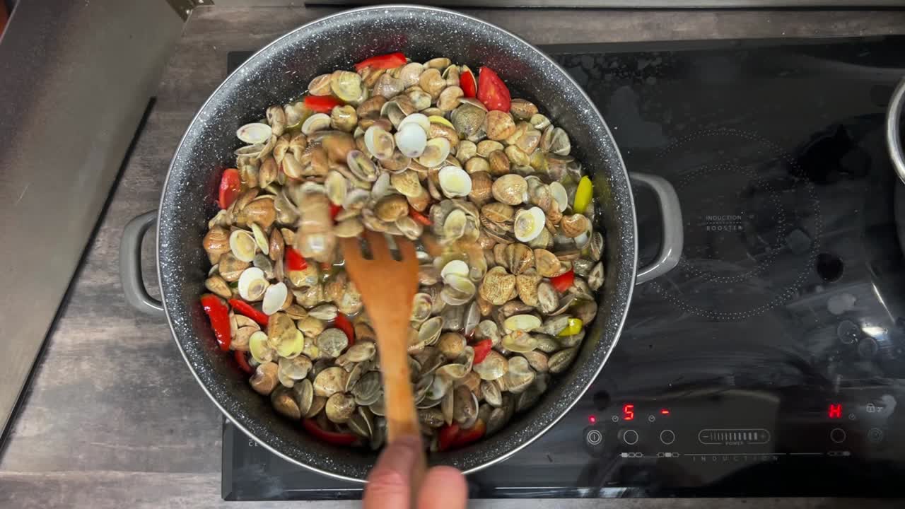Stirring delicious fresh shell clams and red tomatoes with wooden forks in hot pan