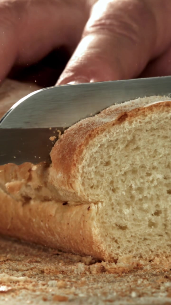 Slicing Freshly Baked Baguette with a Knife, Bread Crumbs Falling