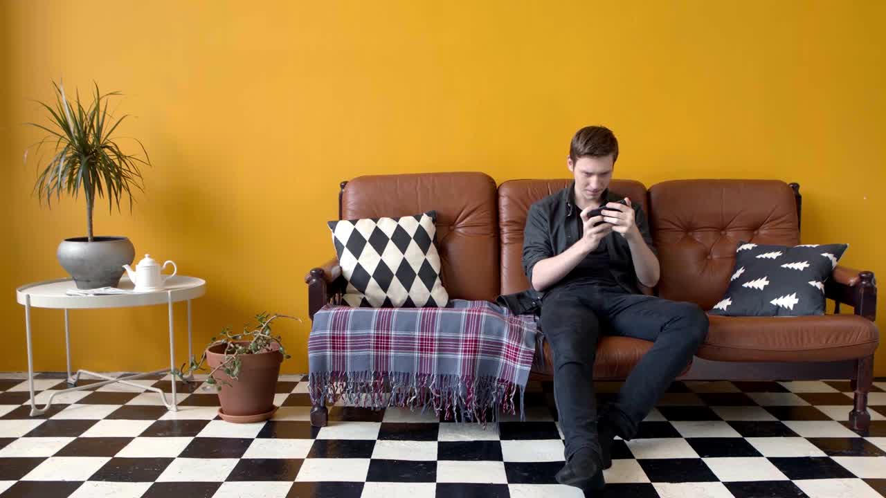 사람 은 거실 에 있는 소파 에 전화 를 사용 하고 있다