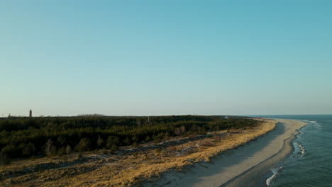 Gentle-waves-at-the-shore-of-Hel-Peninsula,-view-of-forest-and-lighthouse,-Hel,-Poland-aerial