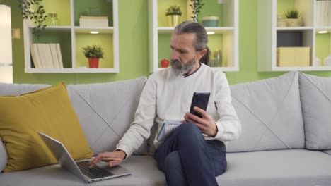 Man-calculating-household-budget-at-home-makes-calculations-using-calculator-on-his-phone.