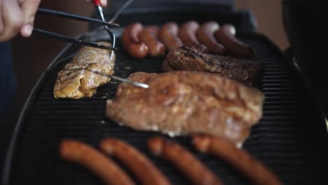 person turning the meat using a fork and tongs on the griller with sausage