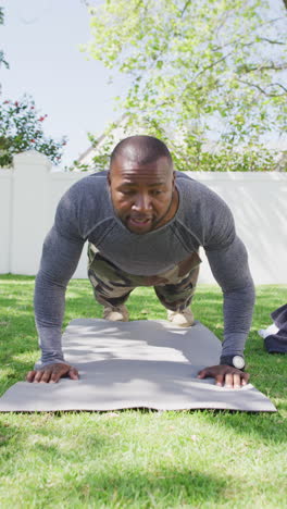 vertical video of african american male soldier exercising, doing push ups in garden