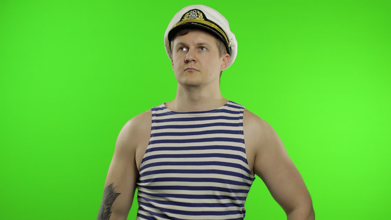 젊은 선원 남자가 손으로 인사를 하고, 위를 올려다보며. 선원의 조끼를 입은 선원 남자