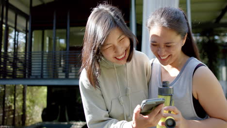 happy asian female friends with water bottle and smartphone laughing on terrace, slow motion