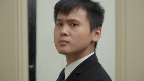 young asian businessman adjusting his suit, smiling, close-up, indoor setting